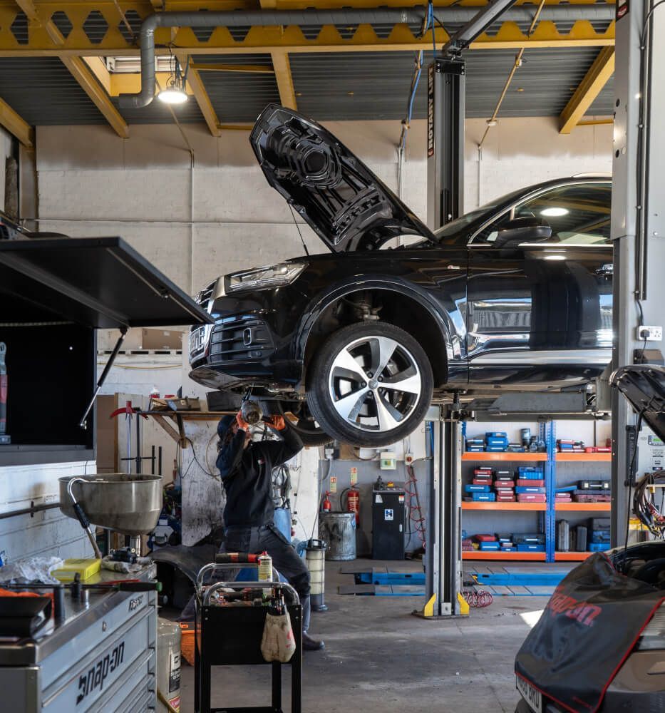 worker under car with car up on stand