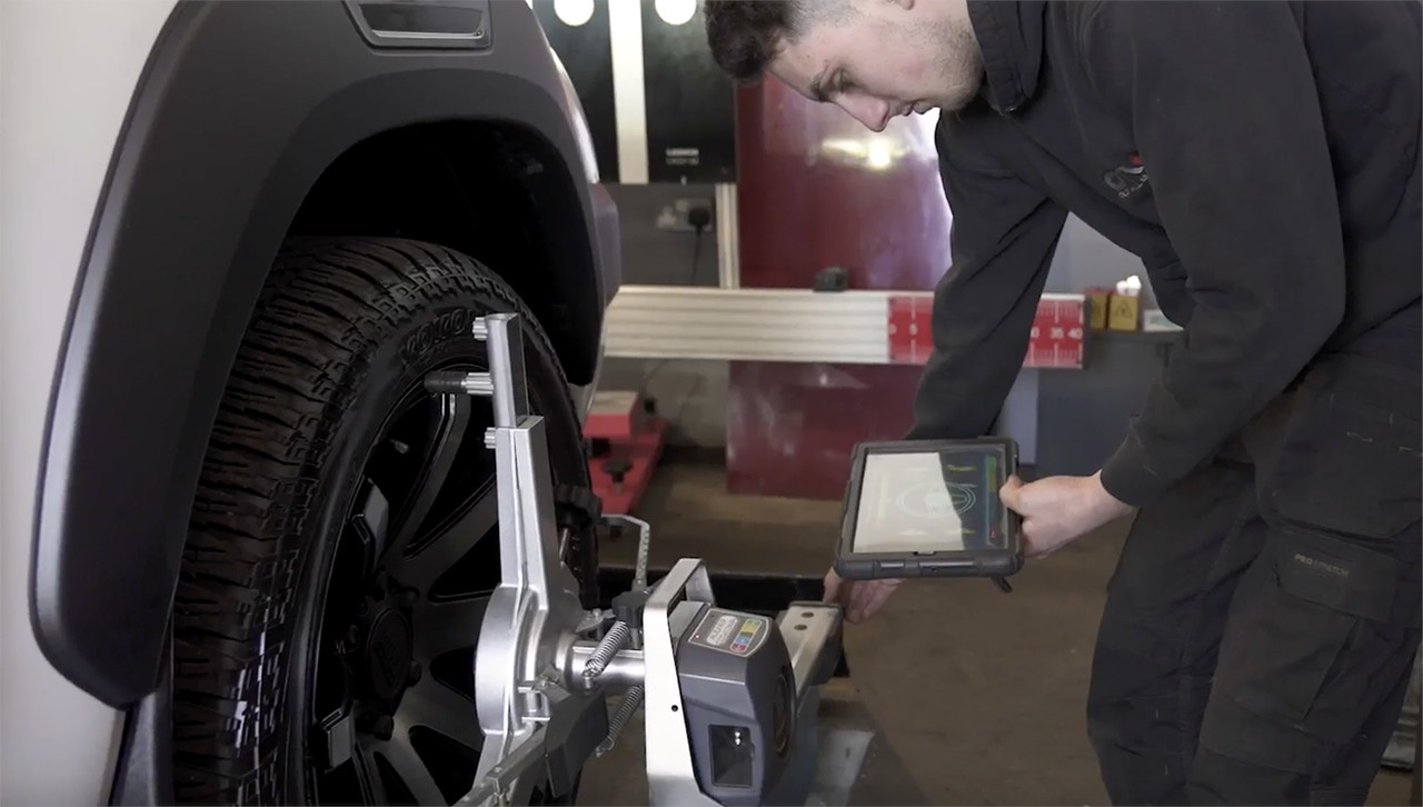 mechanic with wheel alignment tool and tablet with results